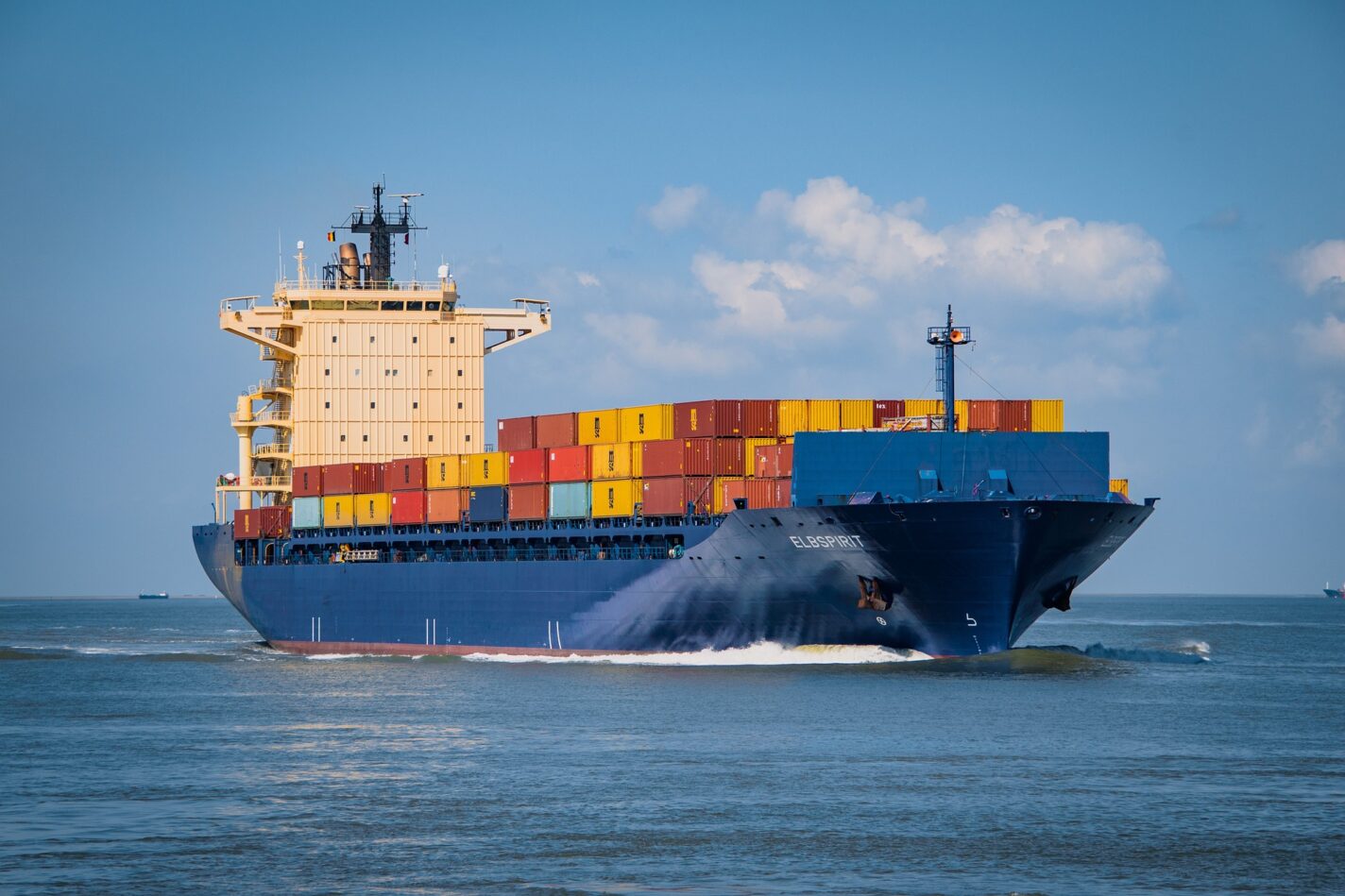 A colorful container ship at sea, with a blue sky behind the ship.