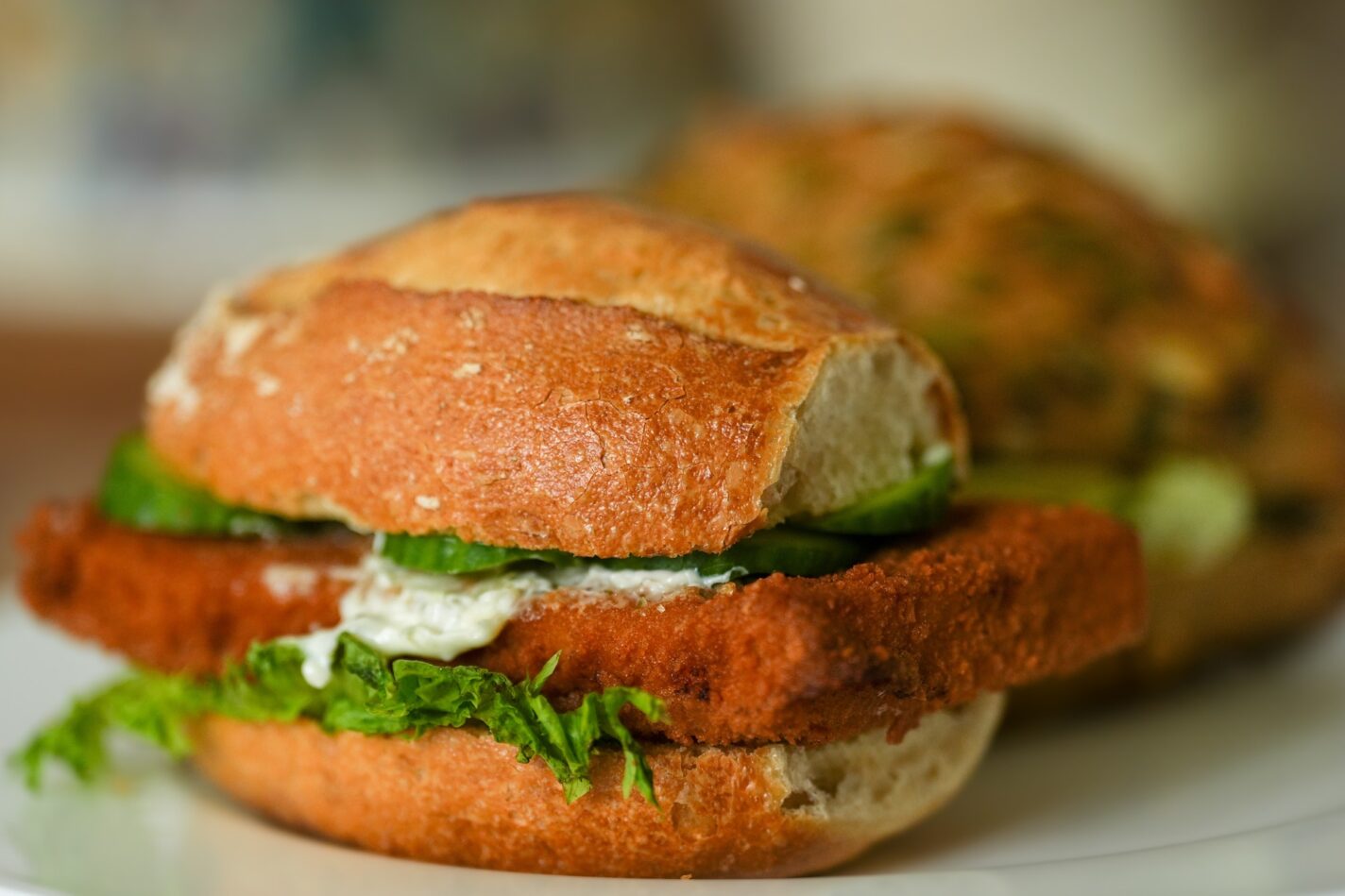 Close-up of a fried fish sandwich with crispy fish fillet, lettuce, and tartar sauce on a toasted bun.